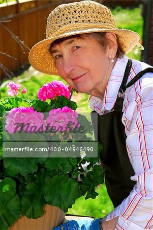 Senior woman with a pot of geranuim flowers in her garden