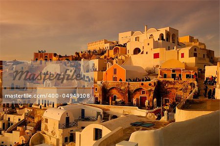 Image shows the traditional village of Oia, on the Greek island of Santorini with hundreds of tourists waiting for one of its famous sunsets