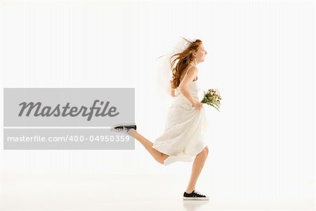 Caucasian bride running and holding bouquet.