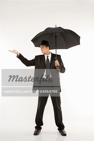 Caucasian mid-adult businessman wearing fedora holding umbrella with arm outstretched.