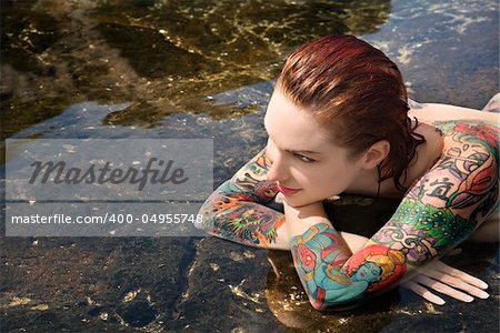 Sexy nude tattooed Caucasian woman lying in tidal pool in Maui, Hawaii, USA.