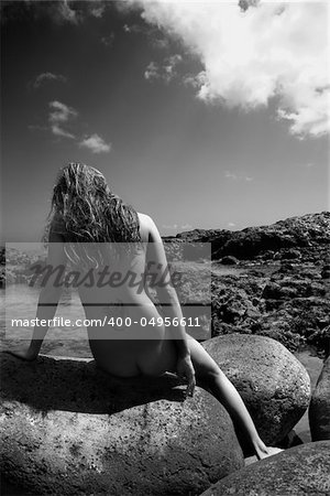 Back view of young nude Asian woman sitting on rocks in Maui, Hawaii.