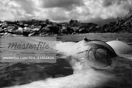 Breast of young Asian nude woman floating on back in water on rocky coast in Hawaii.