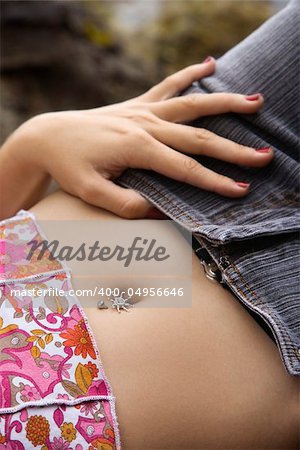 Close up of young Caucasian female lying down with hand on hip and bare midriff.