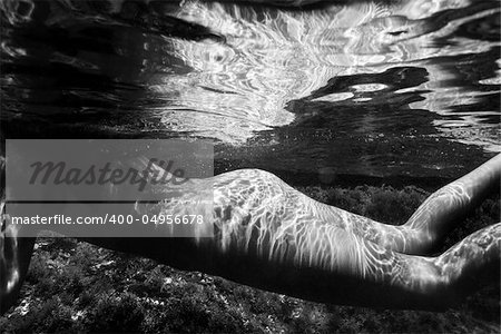 Caucasian young nude female body swimming underwater.