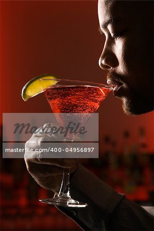 African American man drinking martini in bar against glowing red background.