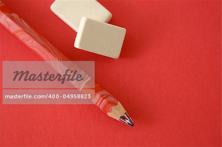 Pencil and two erasers on a red background