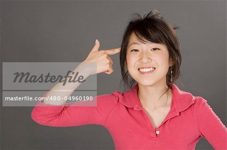 Portrait of a beautiful Asian teenager posing on a gray background with finger pointing at head