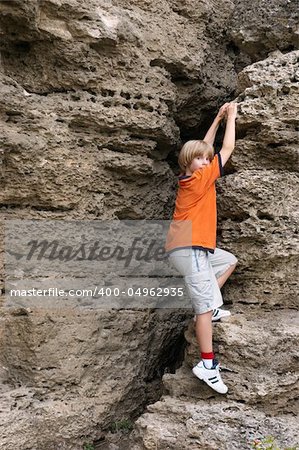 little boy in orange t-shirt climbing on rock