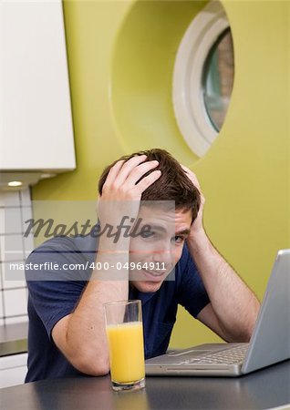 A worried computer user sits in his kitchen with a desperate look on his face