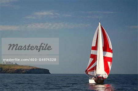 The Yacht with a red sail near island.