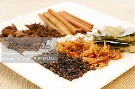 An assortment of fragrant, richly flavored spices - bay leaves, mace, peppercorns, black pepper, silver cardamom pods, cloves and cinnamon. Focus on black peppers.