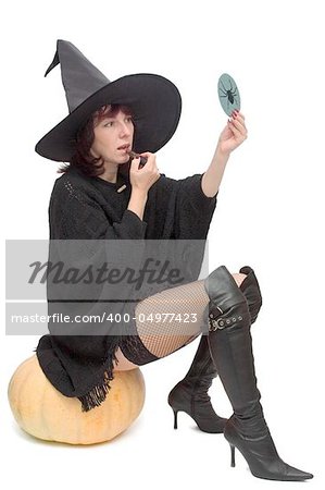 Pretty witch sitting on large pumpkin and making up to prepare for Halloween