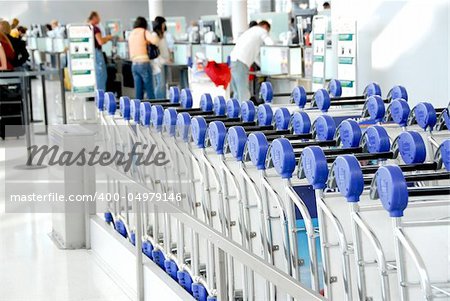 Luggage carts at modern international airport, passengers at check-in counter in the background