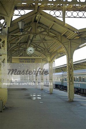 Railroad station platform with a hanging clock, "Have a nice trip" signboard, and two remote human profiles.