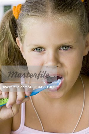 little blond girl cleaning teeth by toothbrush