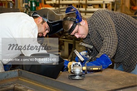 Two welders working together on a difficult metal work project.  Authentic and accurate content depiction in compliance with industry code and safety standards.