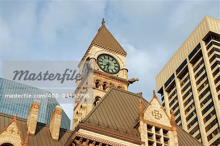 Old city hall of toronto in neo-gothic style between modern skyscrapers under the sunset light