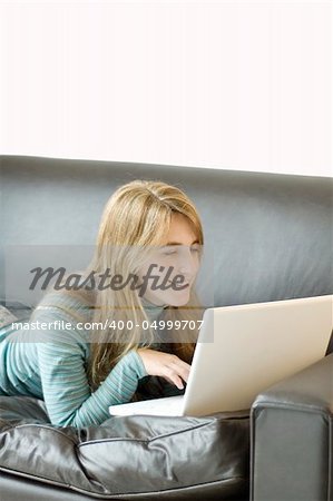 A young woman laying on a sofa with her laptop computer