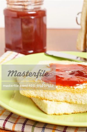 Toast with butter and strawberry jam glass jar in the white plate with soft shadow on square mat background. Shallow depth of field