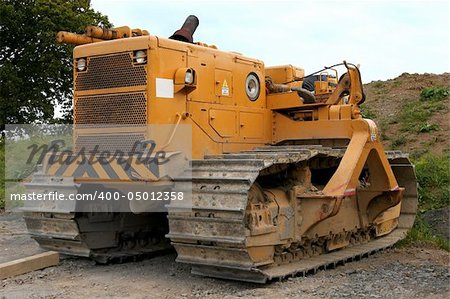 Large yellow bulldozer standing idle on rough earth.