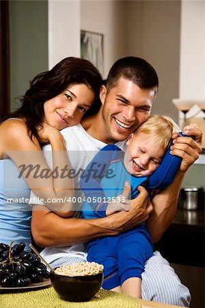 Caucasian family with toddler son in kitchen at breakfast smiling at viewer.