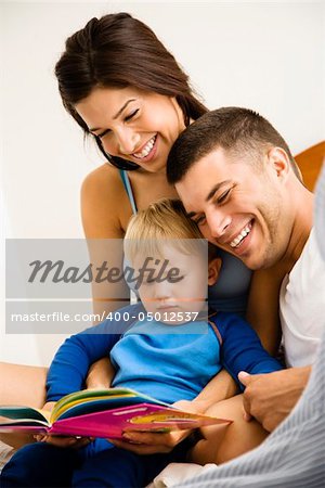 Caucasian parents and toddler son reading book.