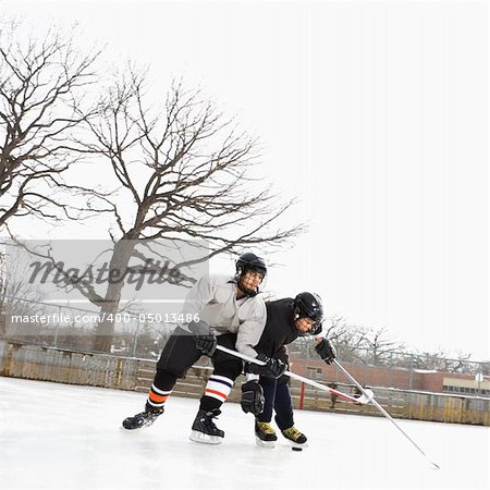 Two boys in ice hockey uniforms playing hockey on ice rink.