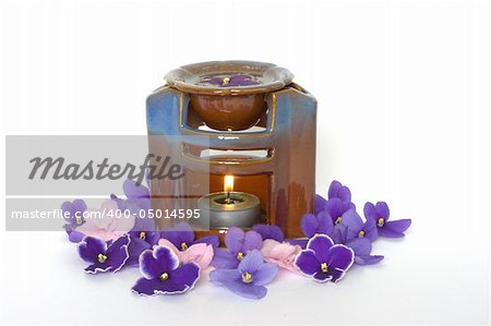 lamp for aromatherapy with burning candle inside surrounded by violet petals