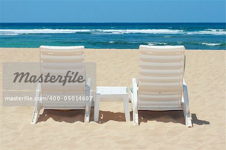 Two sun beach chairs on beach sand near ocean