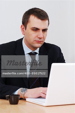 Serious businessman in his office working on white lap-top