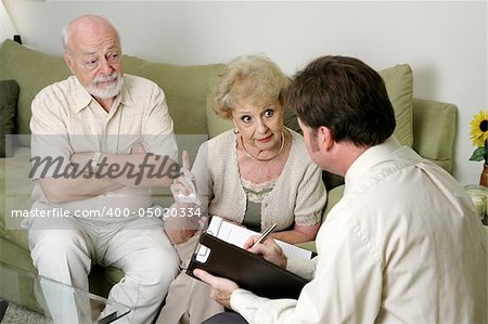 A senior couple in marriage counseling.  She's complaining to the therapist about her husband while he looks on in disbelief.  Focus on wife.