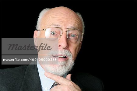A handsome, distinguished looking senior man on a black background looking surprised.