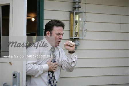 A middle aged man leaving a building and having a coughing fit.