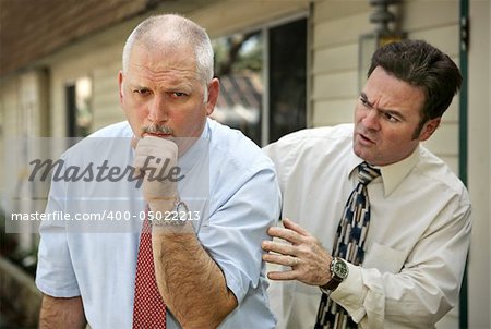 A mature businessman with a severe cough.  His worried colleague is patting him on the back.  Focus on coughing man.