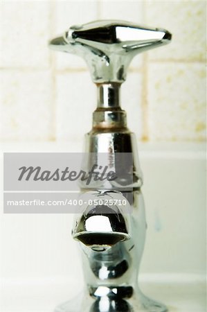 A retro sink tap and faucet with a drip gathering on the end.
