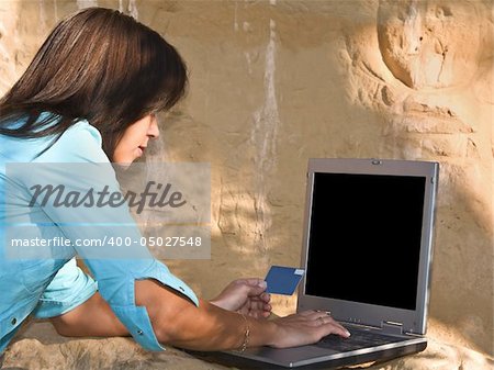 Young woman making an online credit card payment in a rocky environment. Empty latop screen so as you can put what you need on it.