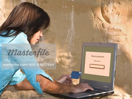 Young woman doing an online credit card payment in a rocky environment.