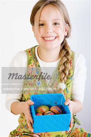 Studio portrait of a young blond girl who is presenting a blue box with her painted easter eggs