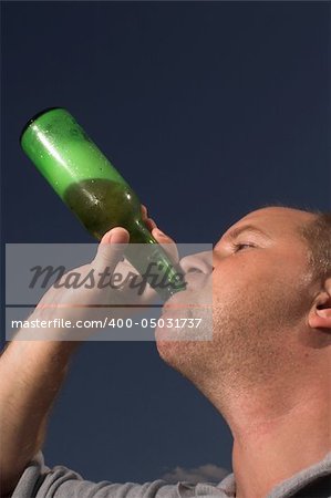 A man drinking a cold beer on a hot day.