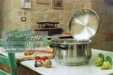 a stainless steel pot on the table with vegetable around