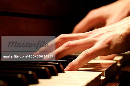 A Caucasian male's hand playing a piano in dramatic lighting