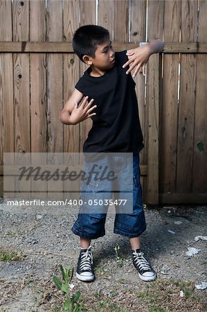Young asian boy standing outside beside a tall wooden fence wearing jeans and black tshirt