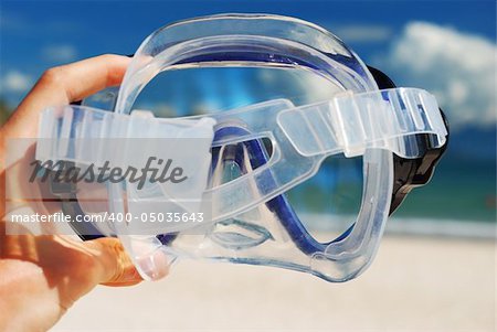 Snorkel equipment in hand against beach and sky