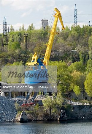 yellow port crane on a river bank ready to load rocks