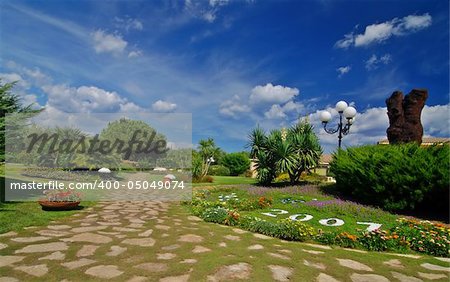 Beautiful park garden with a stone path, many flowers and a blue sky