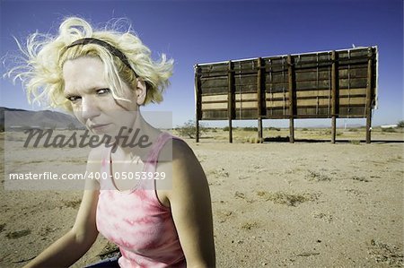Woman with a sour expression in front of an old billboard waiting in the desert.