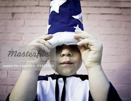 Young boy lifts the brim of a wizard hat and peers out.