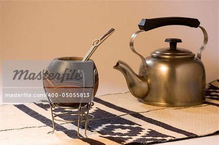 An Argentinean Yerba Mate scene, including a kettle and a typical South American rug. Focus on Mate Gourd