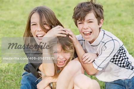 Three young siblings wrestling outdoors on the grass